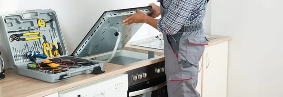 Cooktop repair technician lifting a built-in stovetop for service in Jacksonville, FL